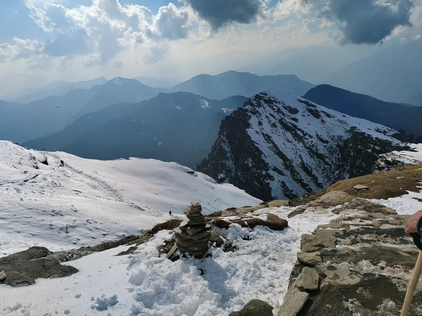 Stone cairn on the snowy Chandrashila summit with ridges beyond