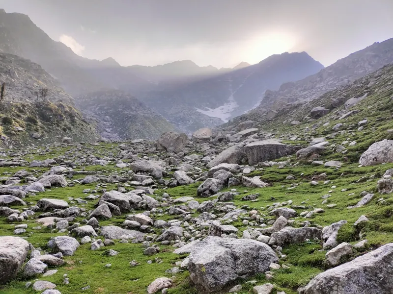 Alpine valley full of boulders and green grass below misty peaks