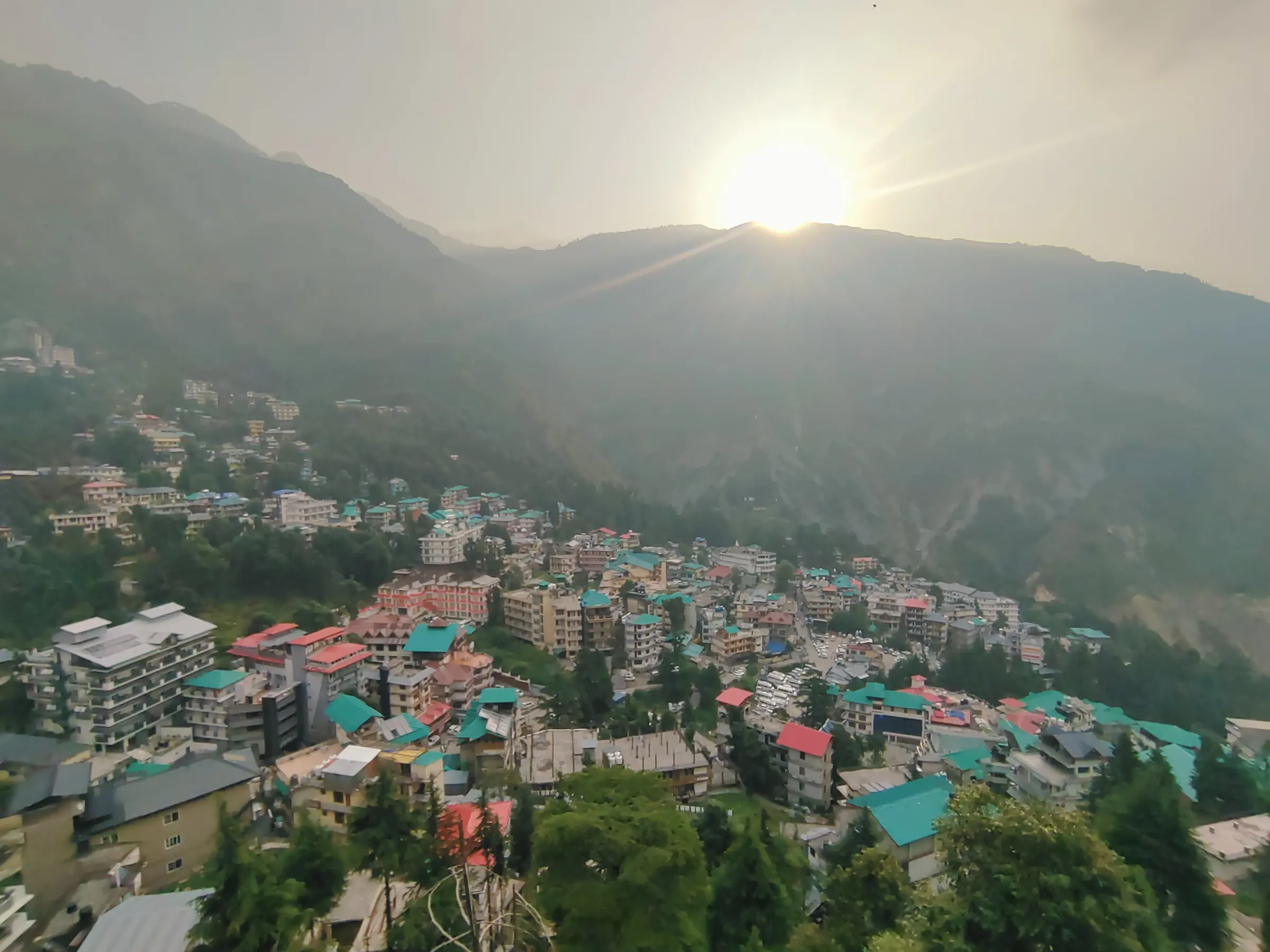 Sunrise over a hill town and forested mountains, seen from above
